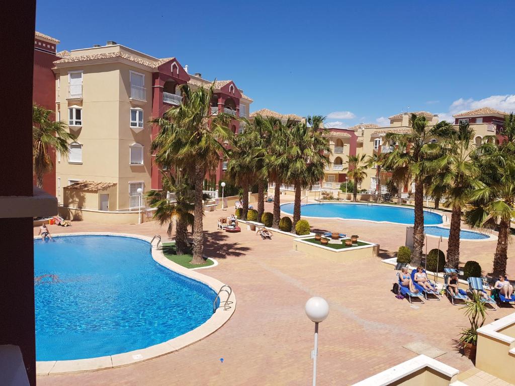 Blick auf einen Pool mit Palmen und Gebäuden in der Unterkunft Casa Ibiza in Los Alcázares