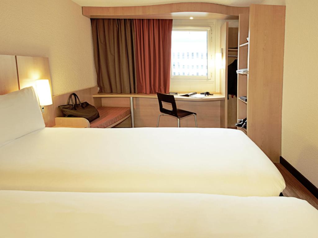 A compact room with a white bed, curtained window, built-in desk and bench seat.