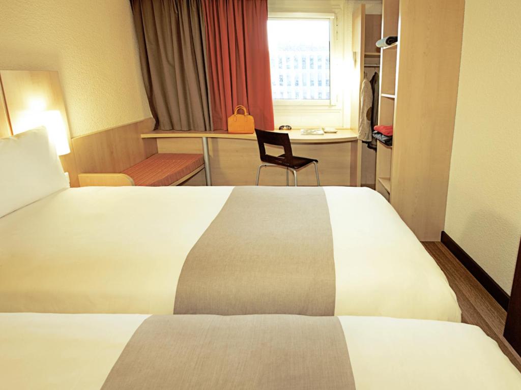 A room with a large bed, built-in work surface, window seat and open storage.