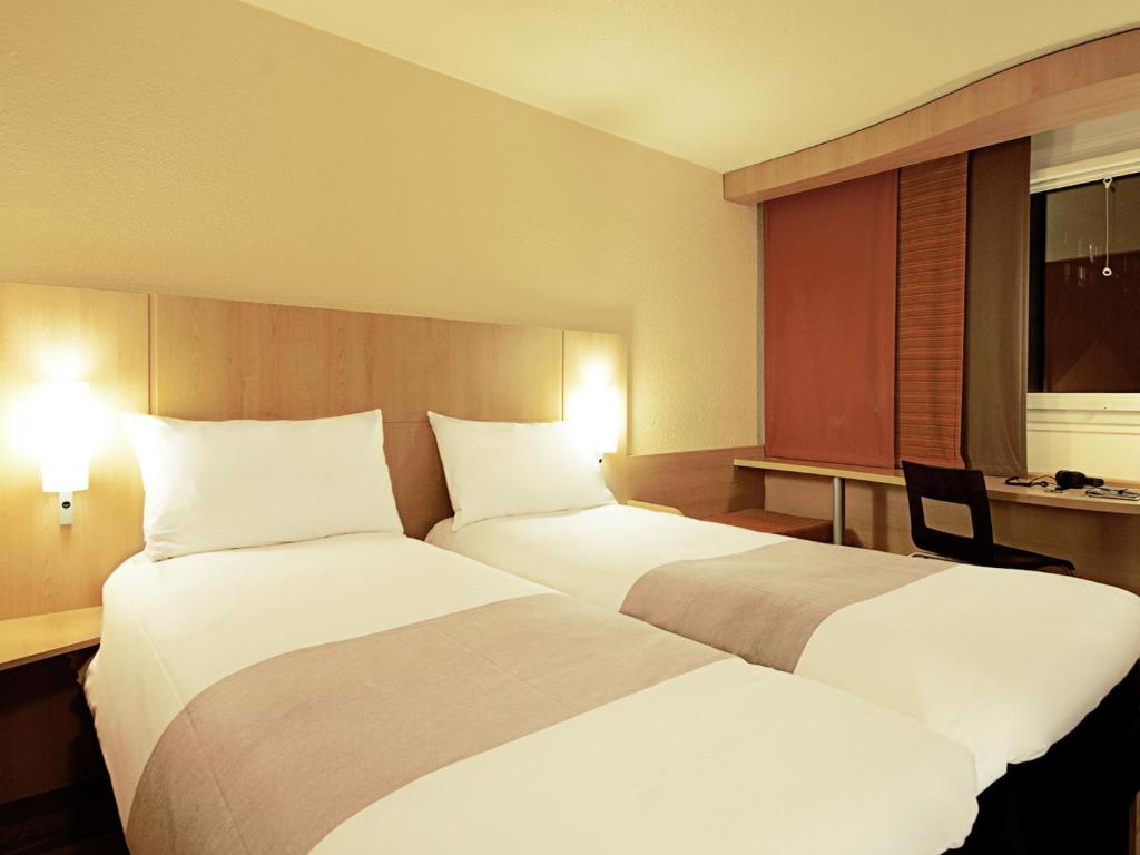 A twin room showing two beds, a built-in desk and a curtained window.