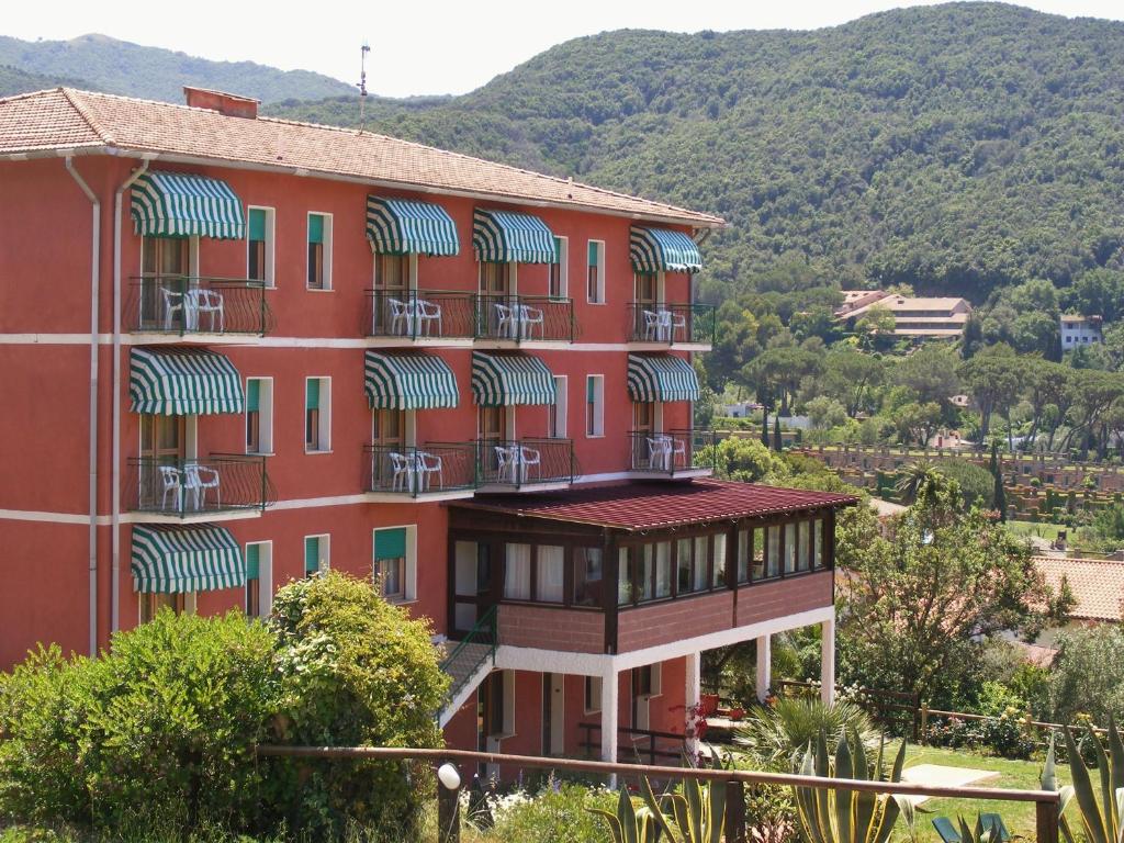 a red building with balconies and a mountain in the background at Hotel La Feluca in Portoferraio