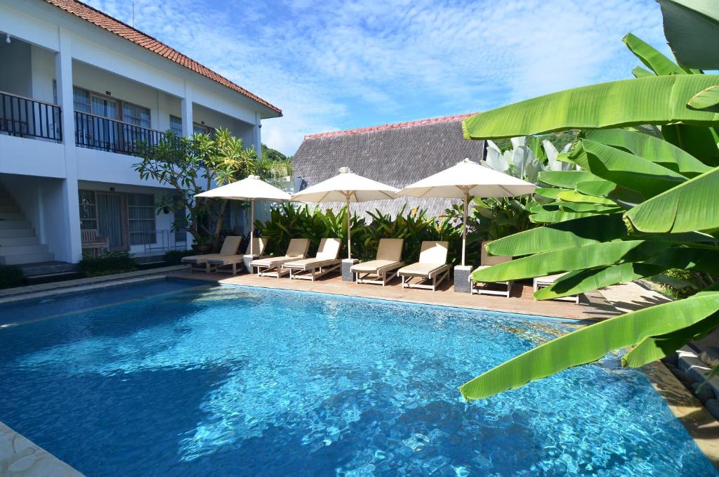 a swimming pool with chairs and umbrellas next to a building at Lavella Villas Kuta Lombok in Kuta Lombok