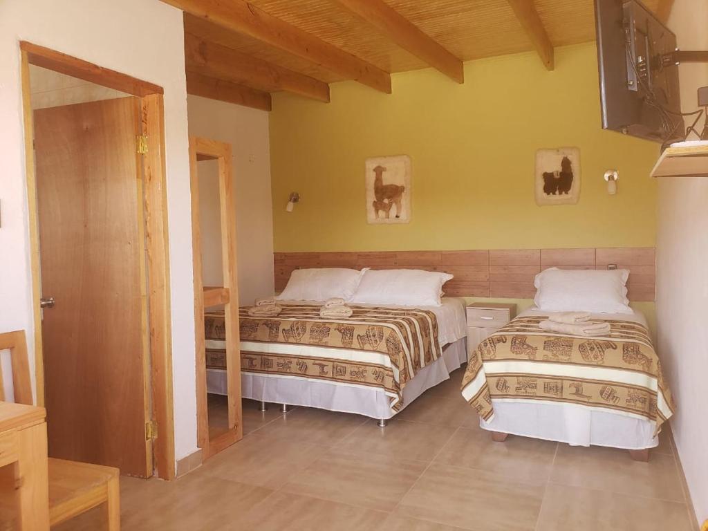 um quarto com duas camas e uma televisão na parede em Hostal Pablito 2 em San Pedro de Atacama