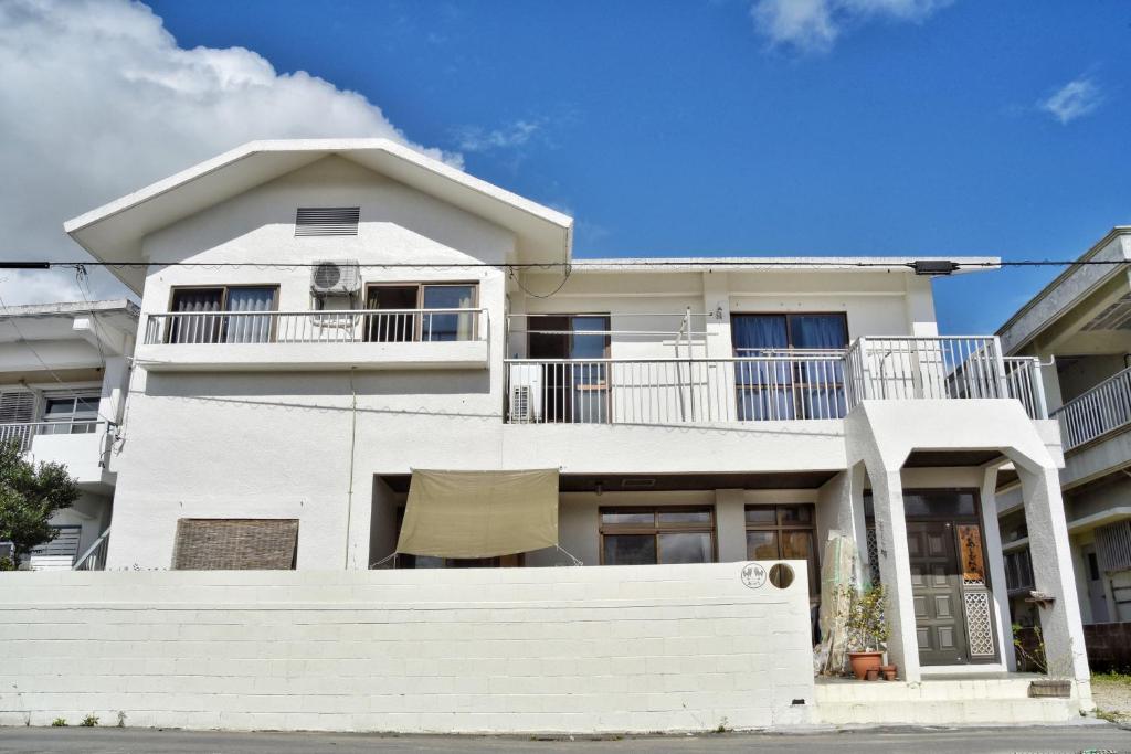 une maison blanche avec un balcon dans une rue dans l'établissement Guesthouse Asibina, à Ishigaki