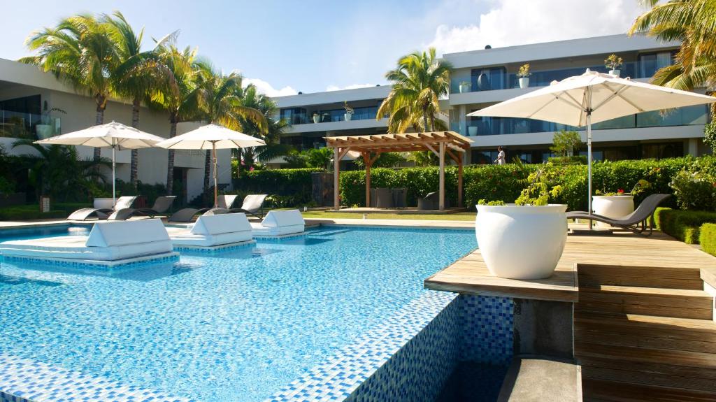 a swimming pool with chairs and umbrellas next to a building at Leora Beachfront by Horizon Holidays in Tamarin