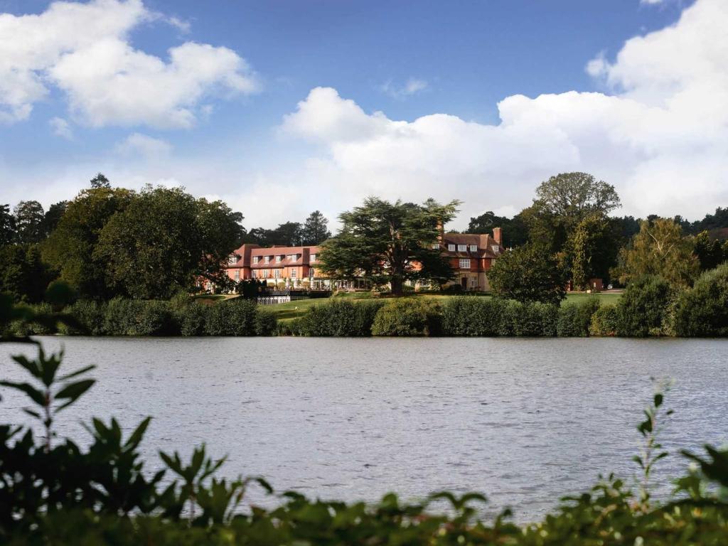 a view of a lake with houses in the background at Champneys Forest Mere in Liphook