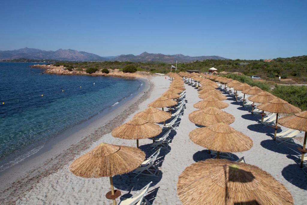 uma linha de guarda-sóis de palha numa praia em Residence Baia Salinedda em San Teodoro