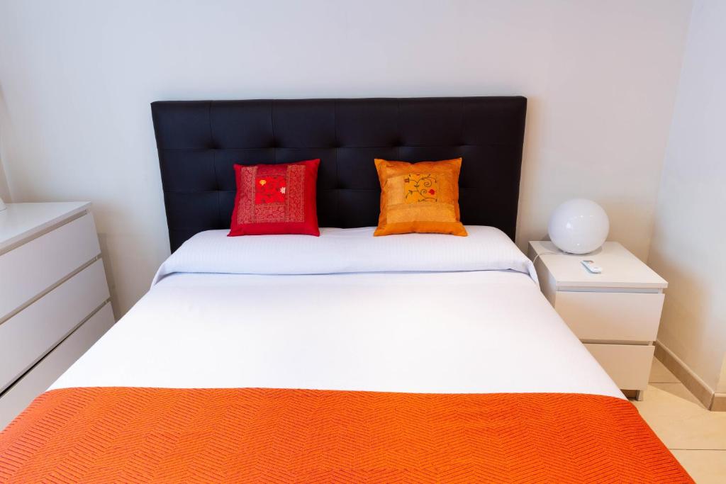 Schlafzimmer mit einem Bett mit orangefarbenen und roten Kissen in der Unterkunft Apartamentos Duque in Madrid