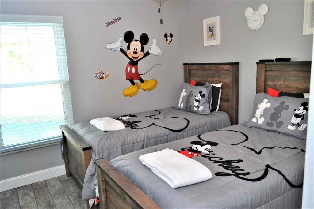 a bedroom with two twin beds with mickey mouse on the wall at Mickeys Landing - Luxurious 4BR with 2 Master Suites, Privacy Fenced Pool & Hot Tub BBQ Game RM 2 miles to Disney! in Orlando