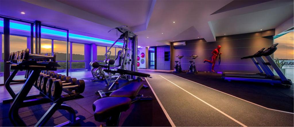A brightly colored hotel gym has cardio machines, weights, and a central running track.
