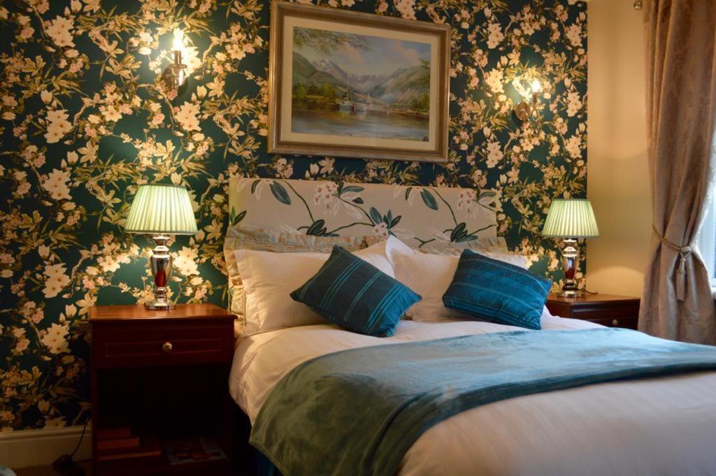 1 dormitorio con cama con almohadas azules y papel pintado con motivos florales en Killyliss Country House B&B, en Lisnalong