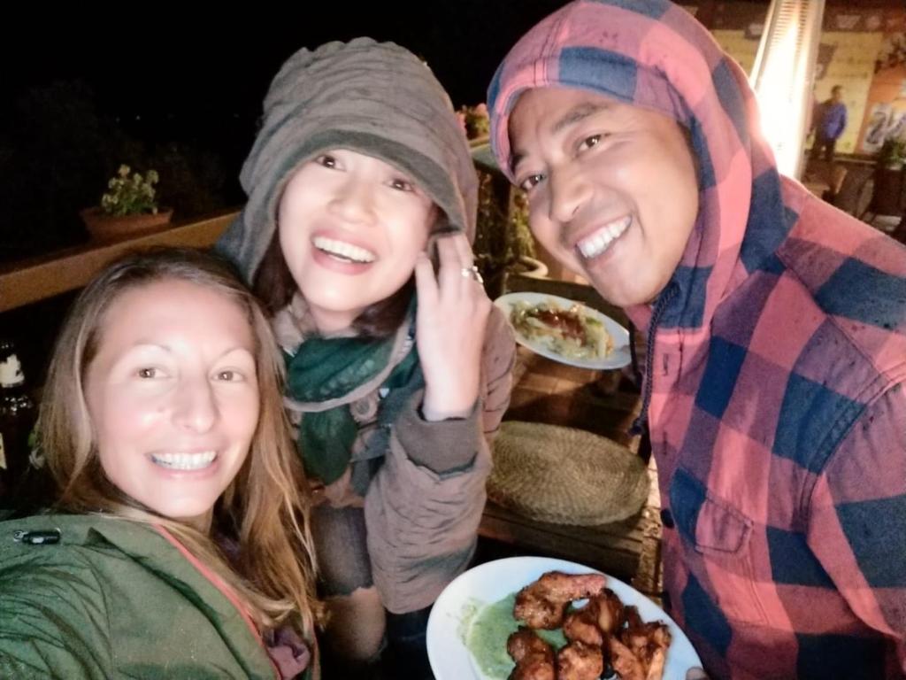 three people posing for a picture with a plate of food at Hotel At The End Of The Universe in Nagarkot