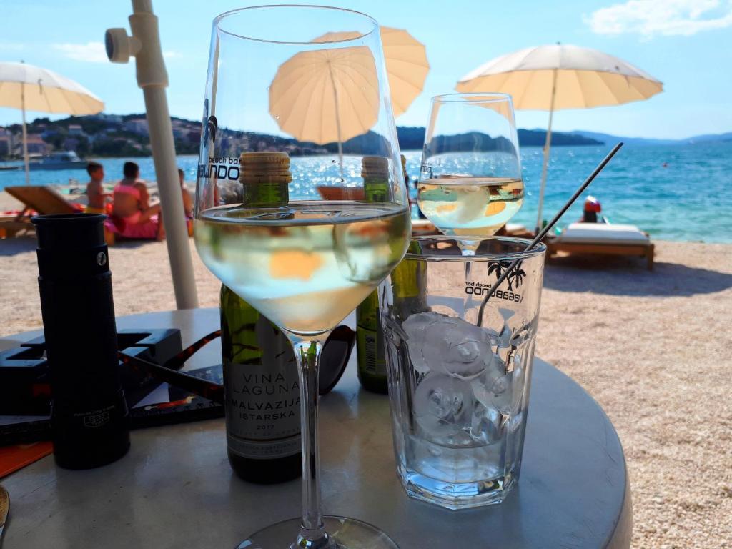 twee glazen witte wijn zittend op een tafel op het strand bij Apartments Infinitas in Trogir