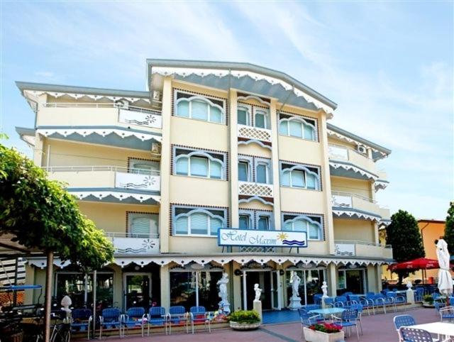 un grand bâtiment avec des chaises bleues devant lui dans l'établissement Hotel Maxim, à Caorle
