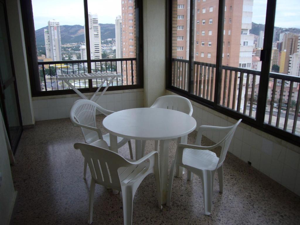 Una mesa y sillas blancas en una habitación con ventanas. en Islandia - Fincas Arena, en Benidorm