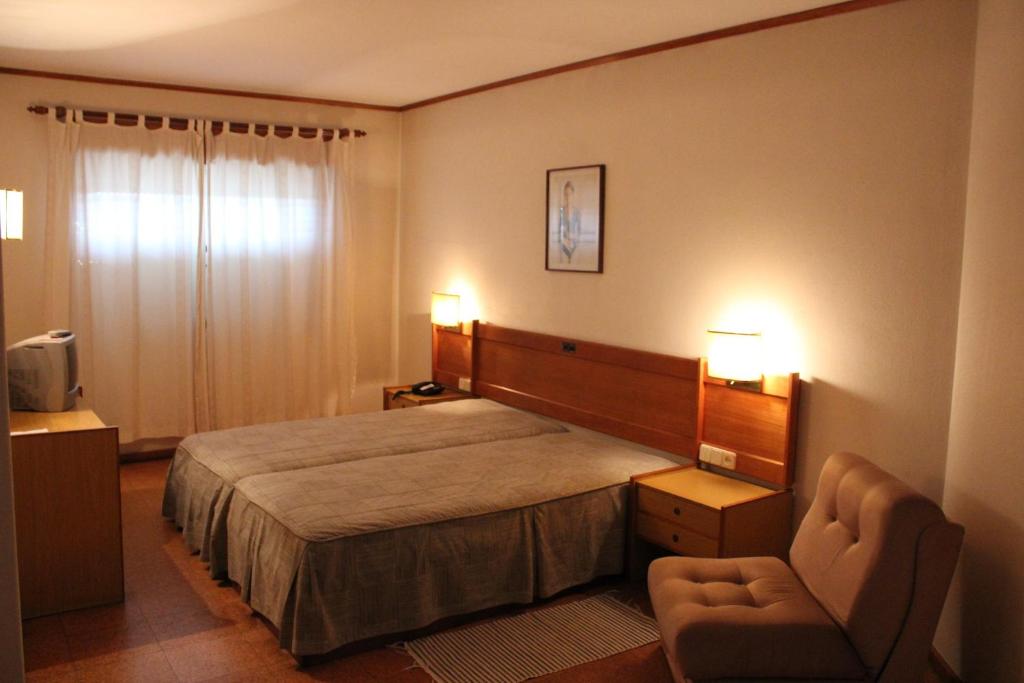 a hotel room with a bed and a chair at Hotel Bom Sucesso in Vila de Prado