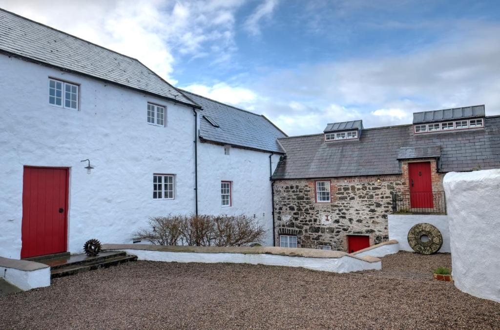 two white buildings with red doors in a yard at Kiln Wing, Old Corn Mill in Bushmills