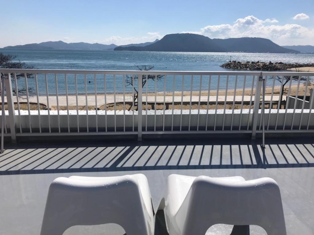 two white chairs sitting on a balcony overlooking the beach at Megijima Island Guesthouse & cafe Megino in Takamatsu