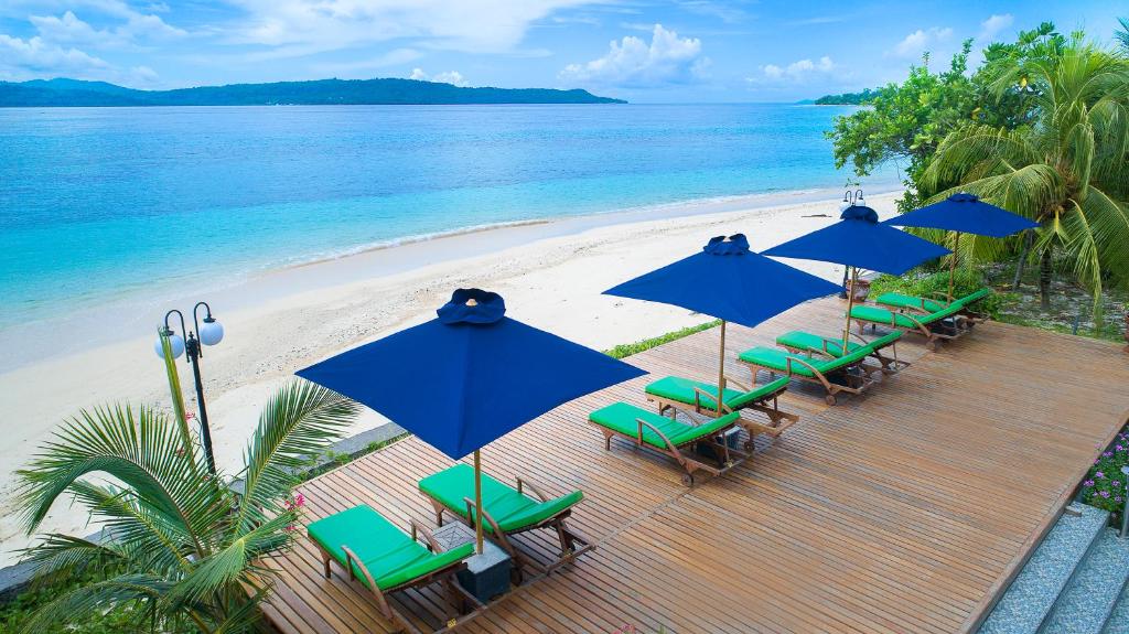 a deck with chairs and blue umbrellas on a beach at Gangga Island Resort & Spa in Serai
