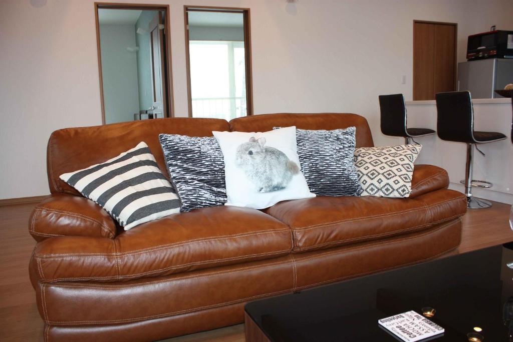 a brown leather couch with pillows with a cat on it at Diamond Dust Furano in Furano