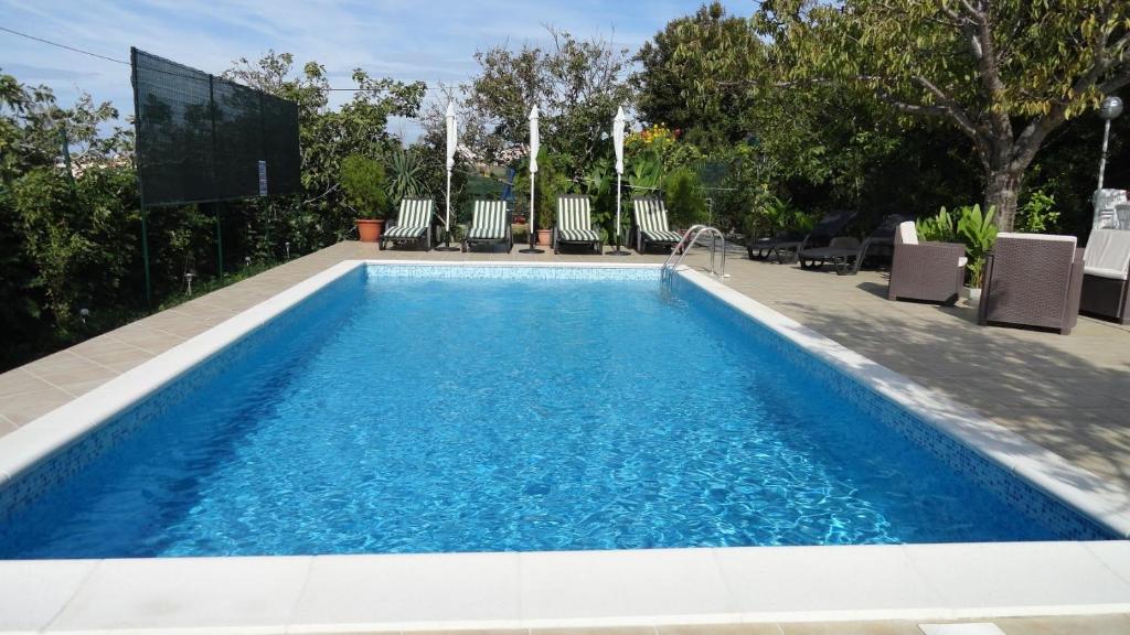 Una piscina con agua azul, sillas y árboles. en Apartments Danijela Rab, en Rab
