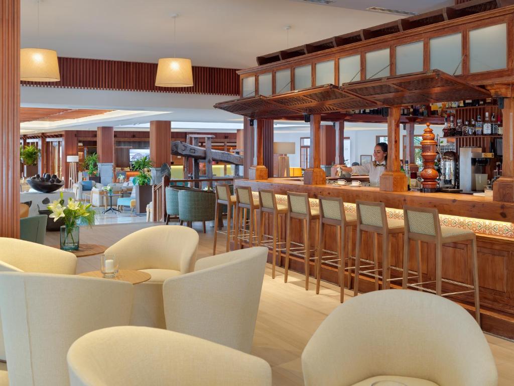 a restaurant with a bar with white chairs and tables at Hotel Jardín Tecina in Playa de Santiago
