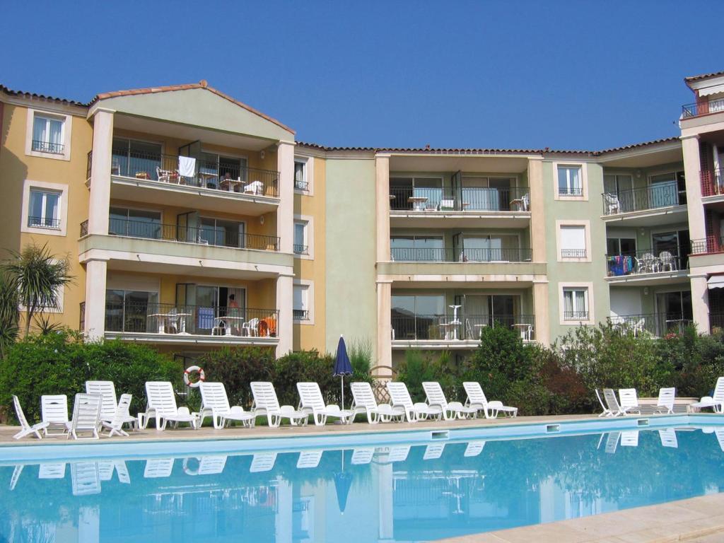 un hôtel avec une piscine, des chaises et un bâtiment dans l'établissement Lagrange Vacances Port-Marine, à Sainte-Maxime