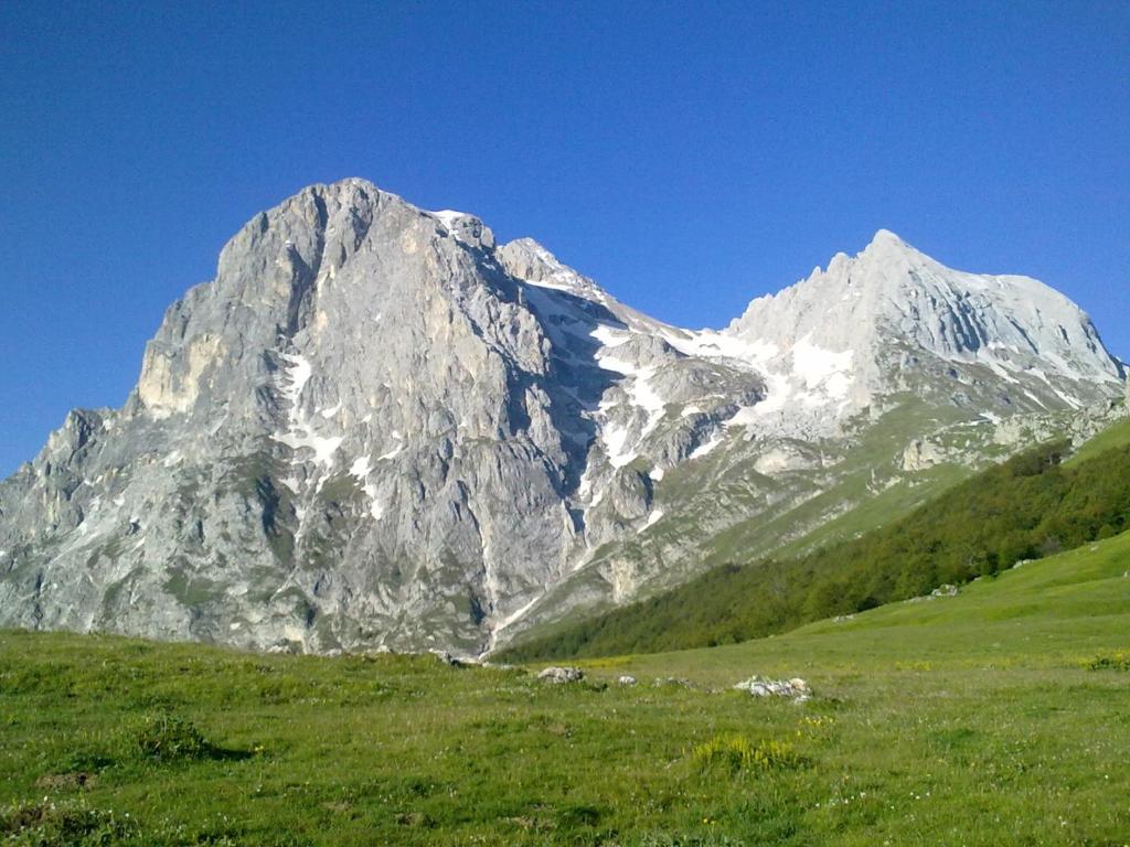 una gran montaña cubierta de nieve con un campo verde en A due passi dal Gran Sasso, en Fano a Corno