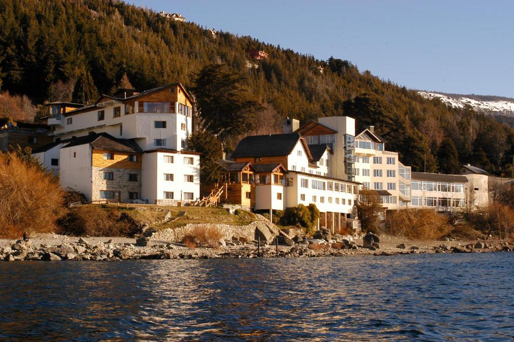 un grupo de edificios a orillas de una masa de agua en Hotel Huemul en San Carlos de Bariloche