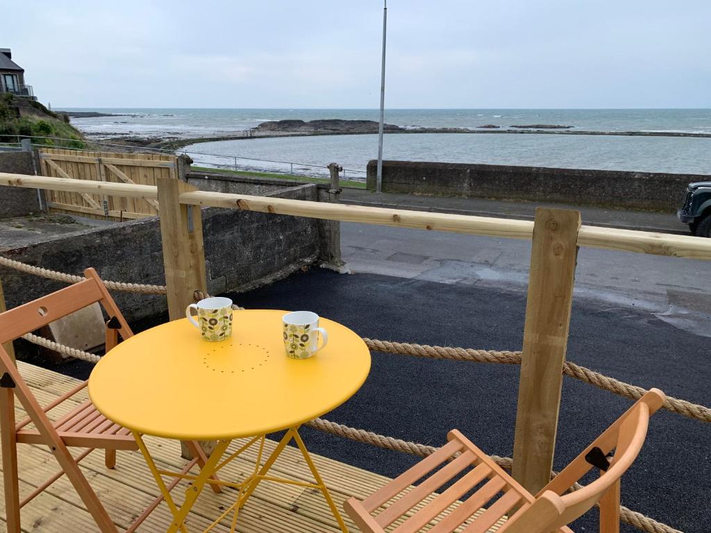 un tavolo giallo e sedie su un balcone con vista sull'oceano di Lagoon View Cottage a Millisle