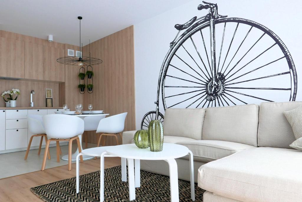 a living room with a white couch and a large wheel on the wall at CHILLIapartamenty - Bliżej Morza - BIKE in Kołobrzeg