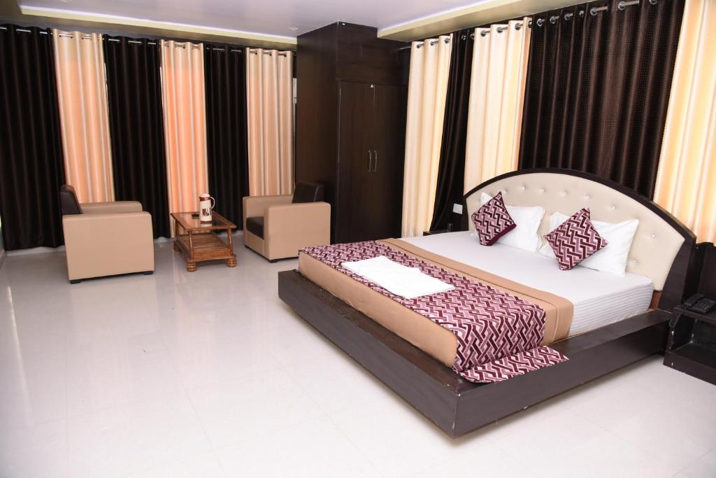 a bedroom with a bed and chairs and curtains at Hotel Mayank in Rewa