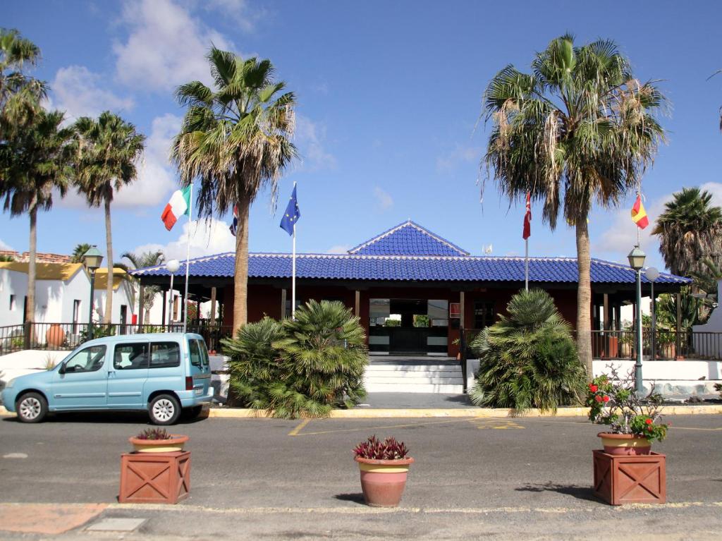a blue car parked in front of a building with palm trees at Casa Anna in Caleta De Fuste