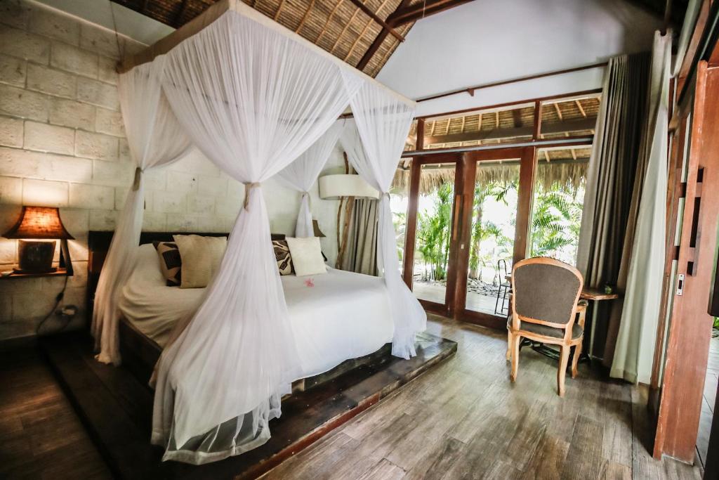 a bedroom with a canopy bed and a chair at La Cabane in Jimbaran
