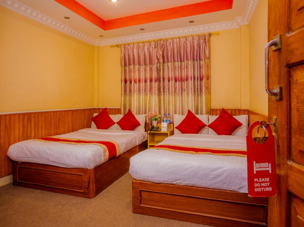 OYO 305 Hotel Gauri في Pashupatināth: غرفة فندق بسريرين ومخدات حمراء