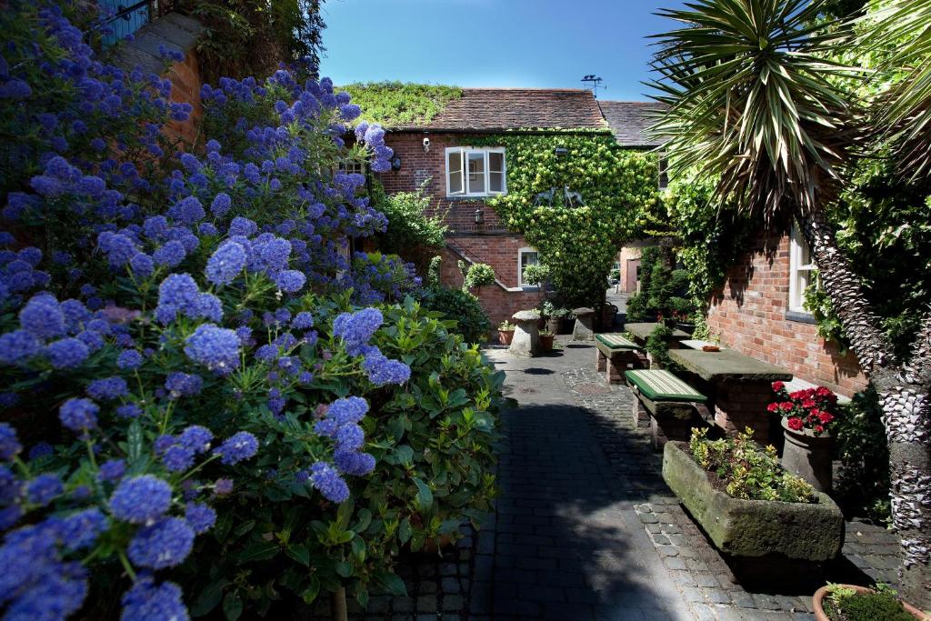 einen Garten mit lila Blumen und Bänken und ein Gebäude in der Unterkunft The Greyhound Coaching Inn in Lutterworth