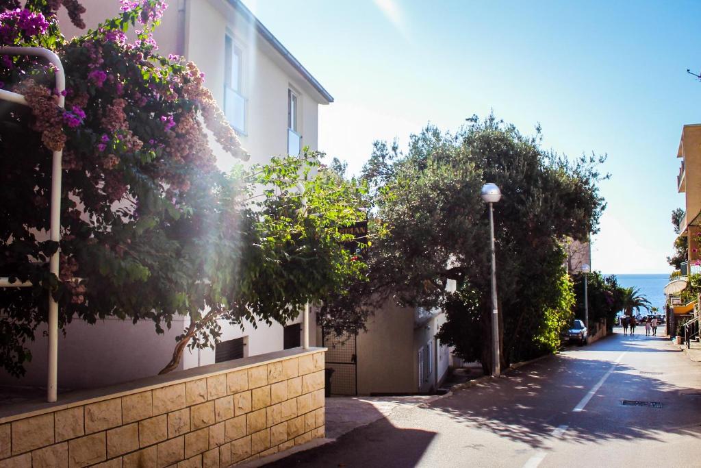 a building with trees and flowers on the side of a street at Apartmani Villa Jasminka in Podgora