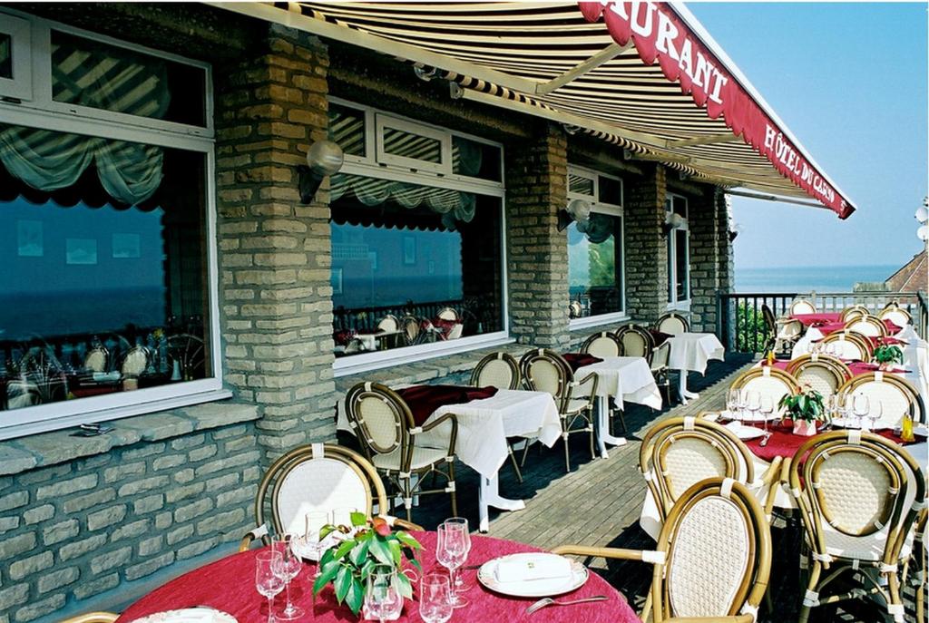 a restaurant with tables and chairs on a deck at Logis Hotel Du Casino Restaurant Le Mathelia in Vierville-sur-Mer