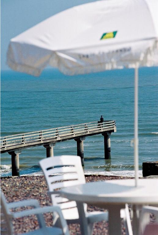a table with chairs and an umbrella on the beach at Logis Hotel Du Casino Restaurant Le Mathelia in Vierville-sur-Mer