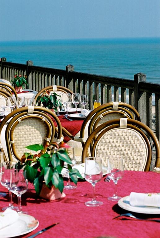 a table with chairs and a table with wine glasses at Logis Hotel Du Casino Restaurant Le Mathelia in Vierville-sur-Mer