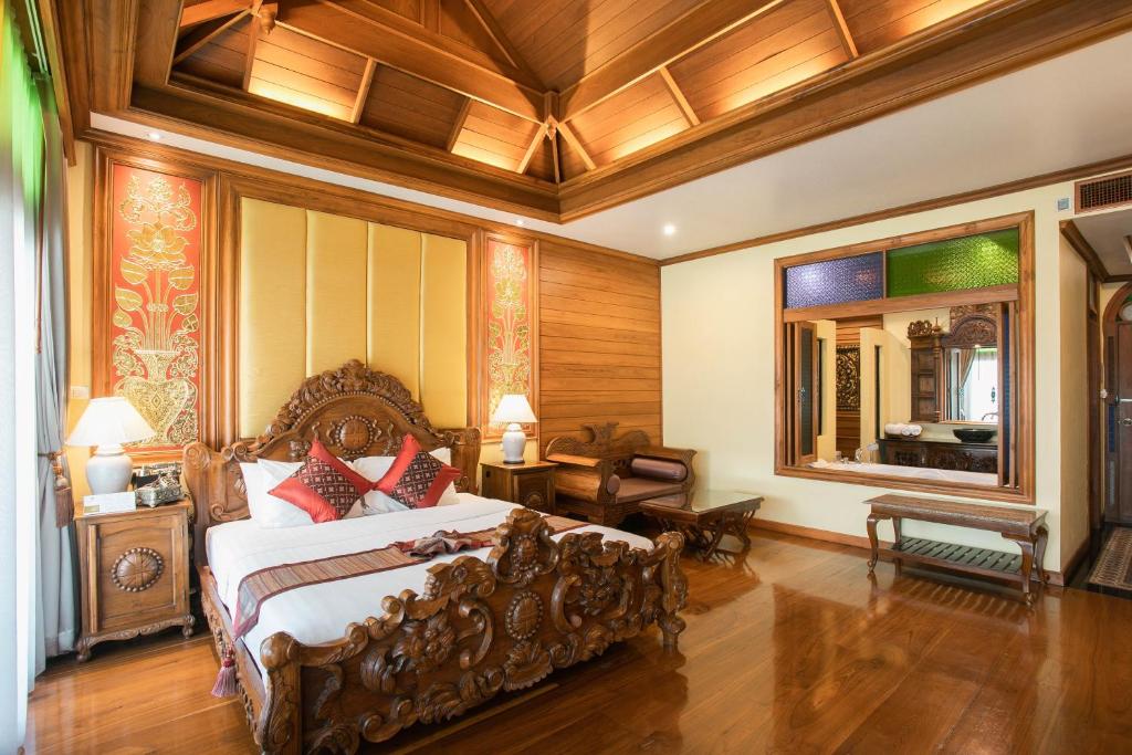 A polished traditional bedroom with an elaborate carved bed, vaulted wood ceiling, and dressing console.