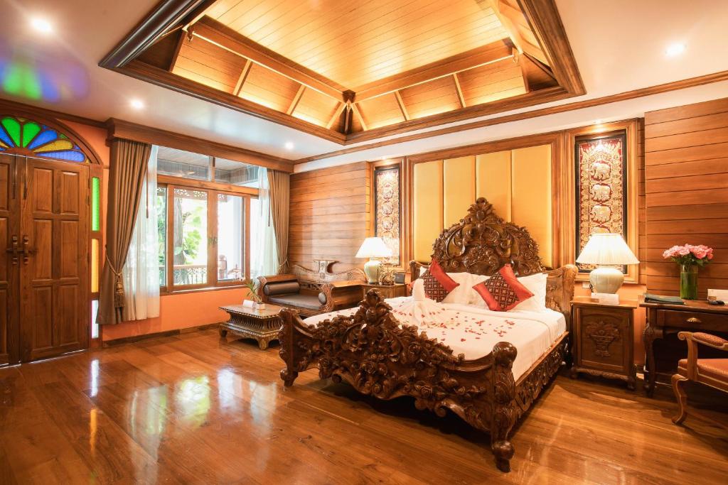 A richly carved bedroom with a large bed, polished wood floors, and a small sitting area.