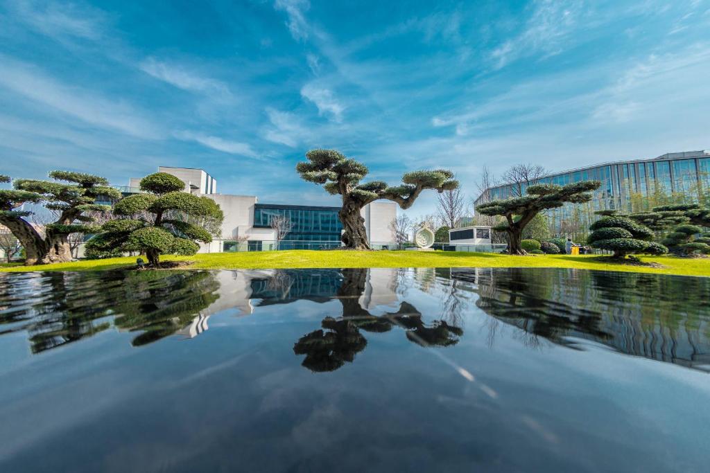 una piscina de agua con árboles frente a un edificio en The Anandi Hotel and SPA - Luxury Healing Hotel for Wellbeing en Shanghái