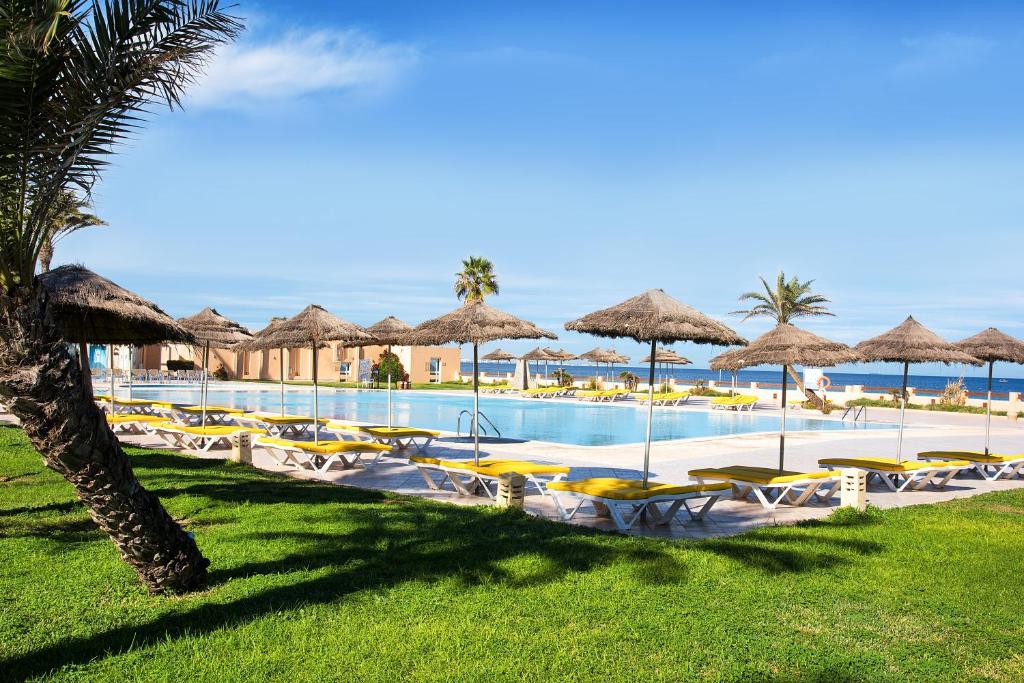 a swimming pool with chairs and umbrellas and the ocean at AQI Skanes Resort in Monastir