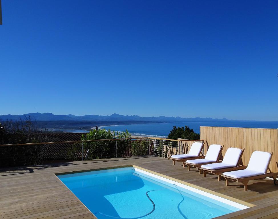 a swimming pool on a deck with lounge chairs and the ocean at Stella Maris Luxury Apartment in Plettenberg Bay