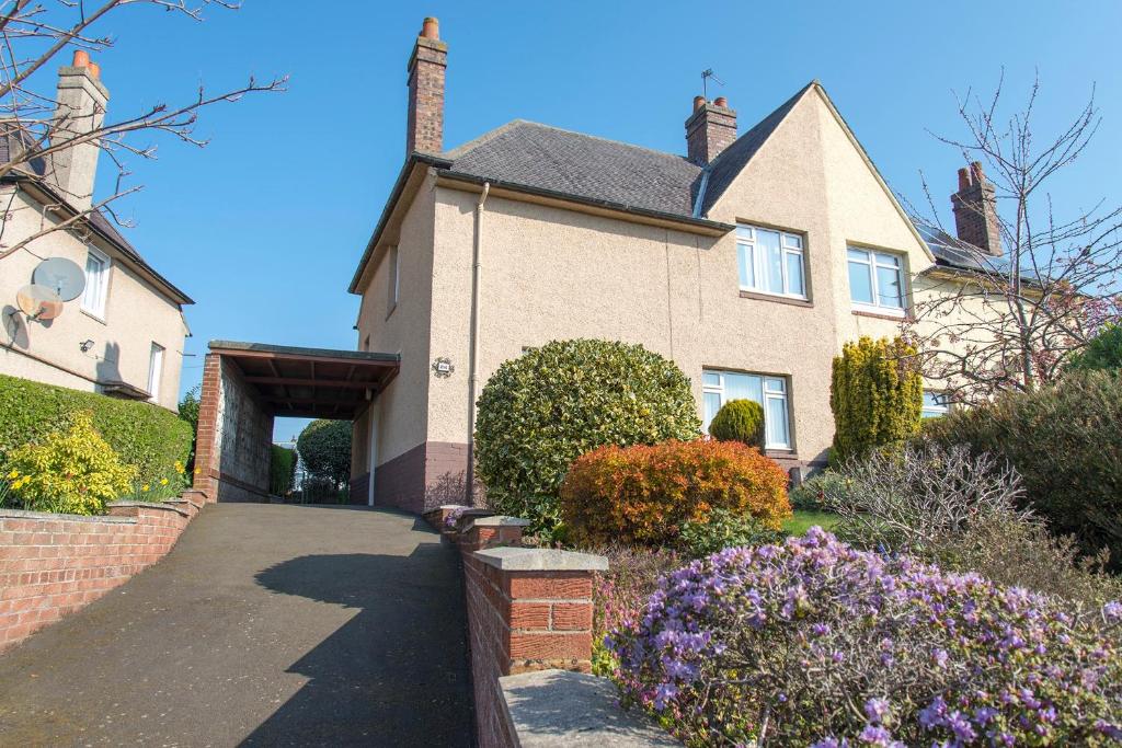 a house with a driveway and flowers in front of it at Park Road Holiday Home in Rosyth