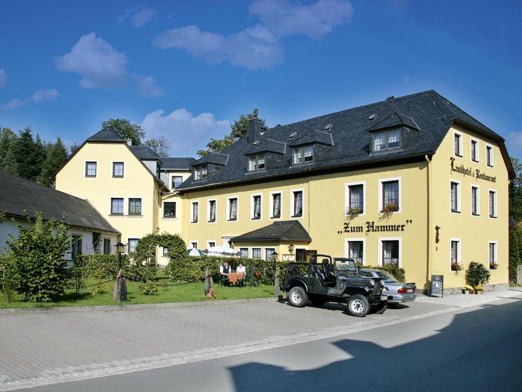 ein großes gelbes Haus mit einem LKW davor in der Unterkunft Landhotel Zum Hammer in Tannenberg