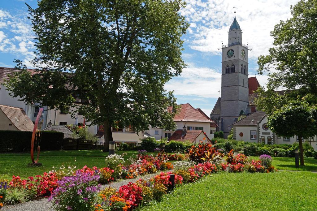 a church with a clock tower and a garden with flowers at Ferienwohnung am Münsterturm in Überlingen