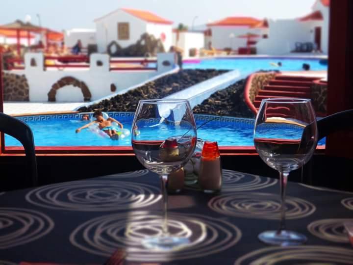twee wijnglazen op een tafel naast een zwembad bij Bungalows Castillo Beach in Caleta De Fuste