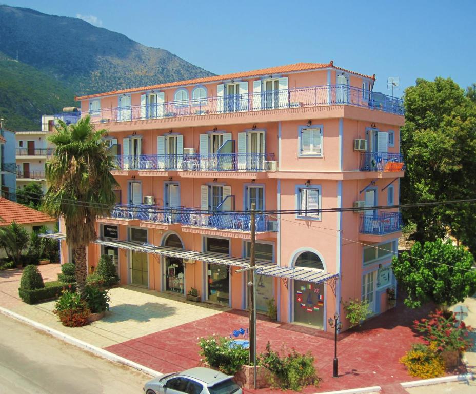 ein rosafarbenes Gebäude mit blauen Balkonen auf einer Straße in der Unterkunft Anemos Studios & Apartments in Póros